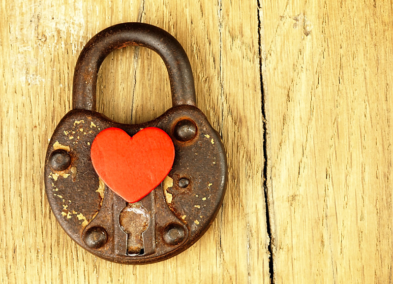 Heart and old rusty padlock with visible surface details on a wooden background.