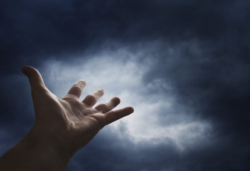 Hand reaching for the  sky with dark stormy clouds